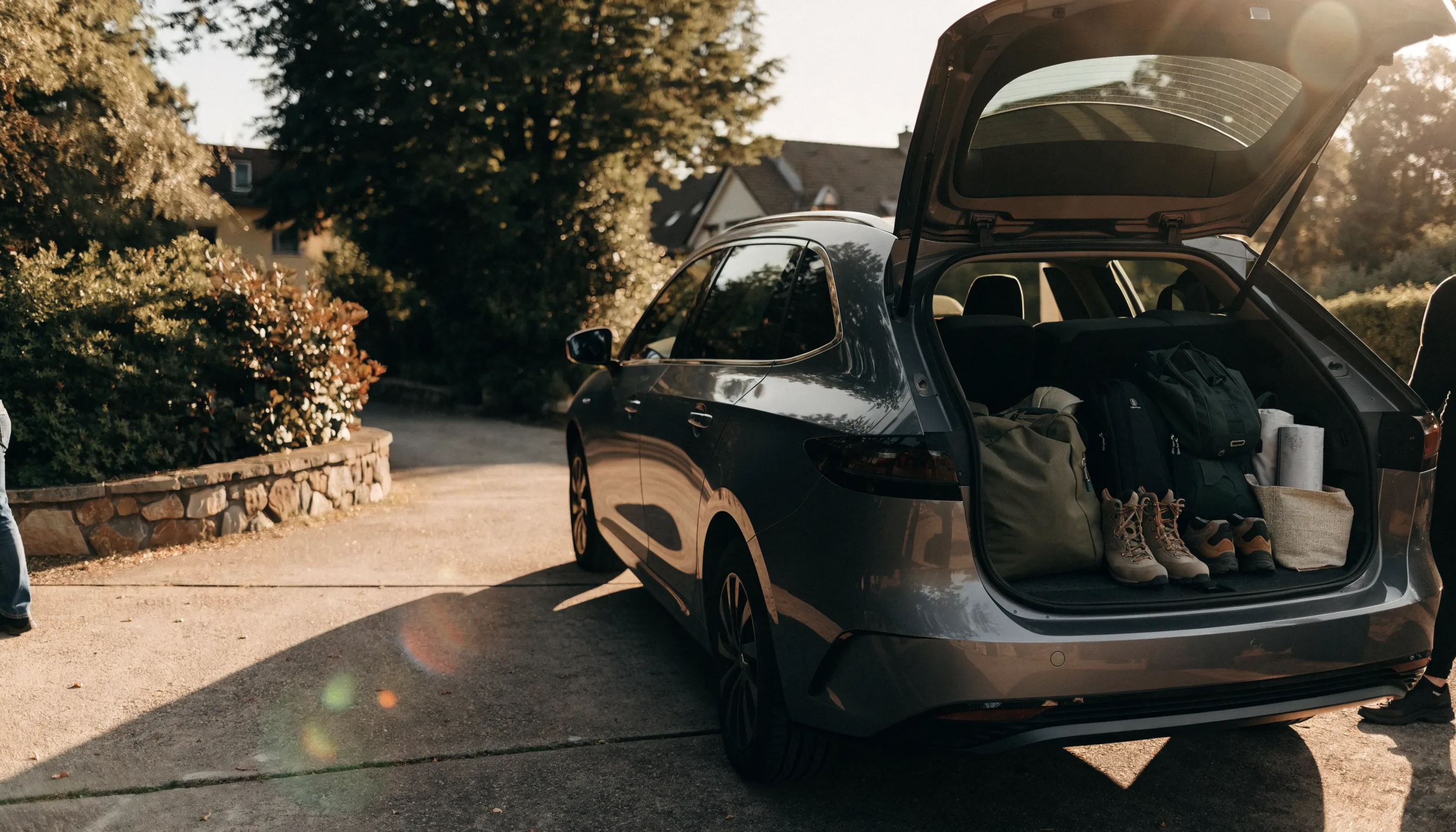 An electric estate car with its boot open on a driveway, packed with luggage and outdoor equipment.