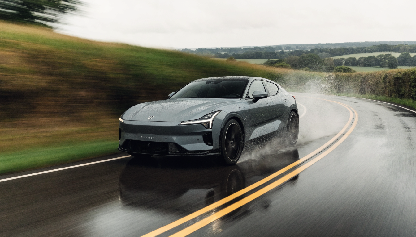 A grey Polestar 4 cornering hard on a wet British B-road, spray lifting from its rear tyres under grey daylight.